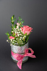 Small vase with pink bow and rose flowers, black background with copy space