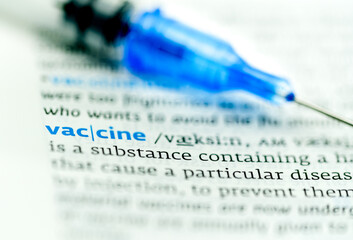 Syringe with covid vaccination lying on dictionary open on the word vaccine
