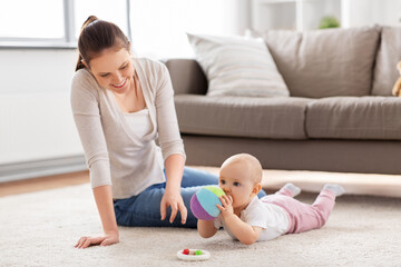 family, motherhood and people concept - happy smiling mother and little baby daughter playing with soft ball toy on floor at home