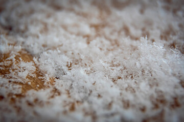 Tiny white snowflakes on a piece of wood. Closeup of snow pattern. Macro photography of geometric texture. Selective focus on the flakes, blurred background.