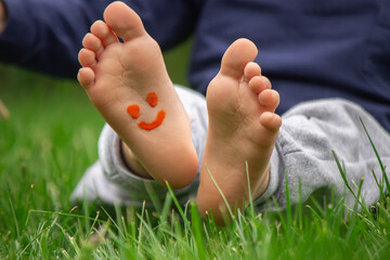 child sitting on the grass, smiling on the child's leg with paints, selective focus