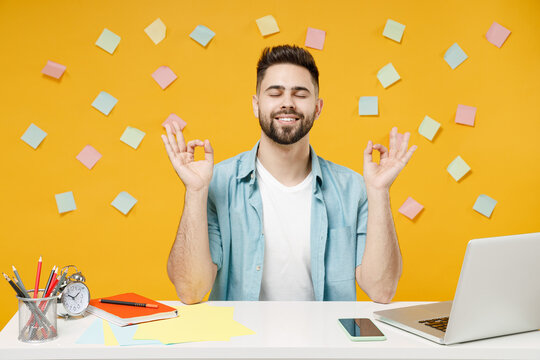 Young employee business man in shirt sit work at white office desk with pc laptop hold spread hands in yoga om gesture relax meditate try to calm down isolated on yellow background studio portrait