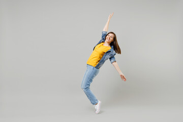 Full length side view young caucasian woman in casual denim jacket yellow tshirt looking camera leaning back stand on toes dancing isolated on grey background studio portrait People lifestyle concept