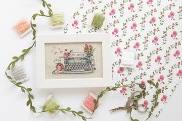 cross stitch typewriter saying hello spring on linen canvas in white frame, floss threads on...