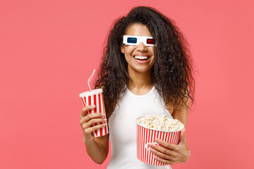 Young fun smiling african woman 20s in 3d glasses watch movie film hold akeaway bucket of popcorn cup of soda isolated on pink background studio portrait. People emotions in cinema lifestyle concept