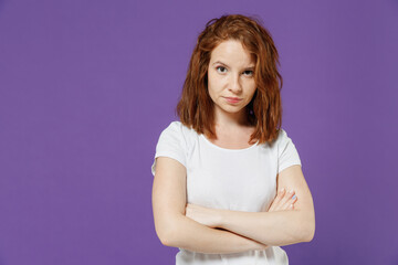 Young serious frowning offended sad shrewd indignant caucasian woman 20s in white basic casual t-shirt looking camera holding hands crossed folded isolated on dark violet background studio portrait