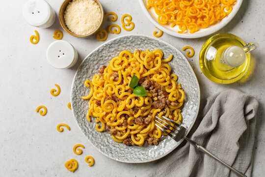 Pasta Gramigna uncooked and cooked whith sausage - gramigna alla salsiccia. Parmesan cheese and olive oil. Classic italian food. Top view.