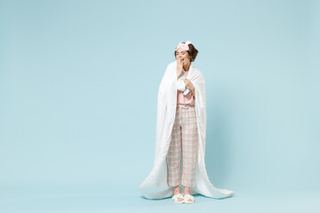 Fototapeta na wymiar Full length young sleepy fun woman in pajamas jam sleep eye mask rest relax at home wrap covered under blanket duvet yawning isolated on pastel blue background studio Good mood night bedtime concept.