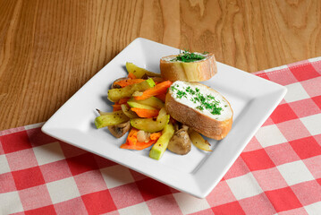 Roasted vegetables served in a white square plate over red plaid table cloth