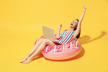 Full body length happy young sexy woman wear red blue swimsuit sit on inflatable ring work on pc laptop isolated on vivid yellow color background studio Summer hotel pool sea rest sun tan concept