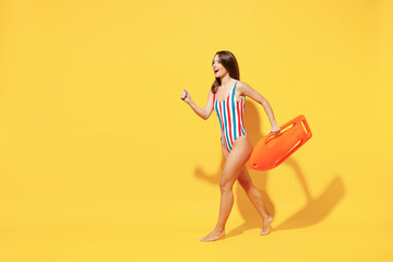 Full length fun happy sexy woman slim body wear red blue one-piece swimsuit jump high air run fly hold lifebuoy isolated on vivid yellow color background studio Summer hotel pool sea rest sun concept