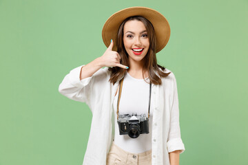 Traveler tourist woman in casual clothes hat camera on neck doing phone gesture says call me back isolated on green background. Passenger travel abroad on weekends getaway. Air flight journey concept.