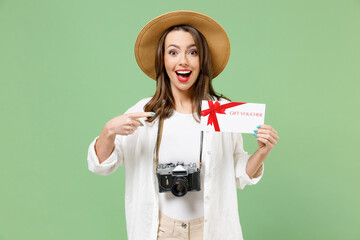 Traveler fun tourist woman in casual clothes hat camera point finger on gift voucher flyer mock up isolated on green background Passenger travel abroad on weekends getaway. Air flight journey concept.
