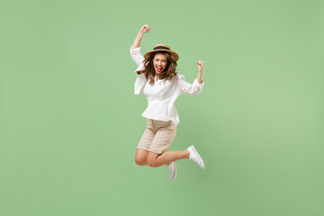 Full length traveler tourist woman in casual clothes straw hat jump high do winner gesture isolated on pastel green background. Passenger travel abroad on weekends getaway. Air flight journey concept.