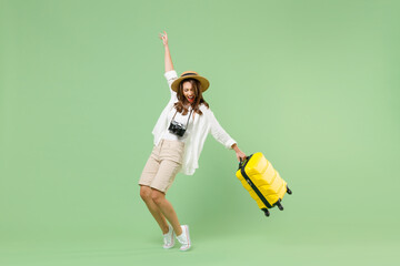 Full length traveler tourist woman in casual clothes hat hold suitcase stand on toes dance lean back isolated on pastel green background. Passenger travel abroad weekends. Air flight journey concept. - Powered by Adobe
