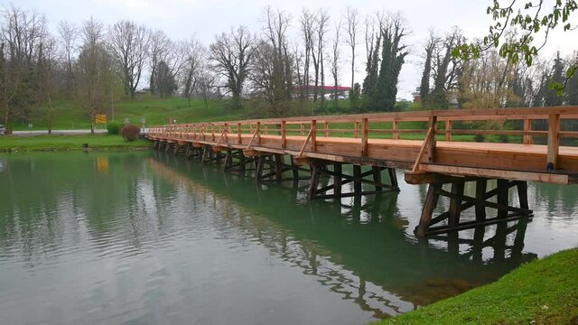 Empty wooden bridge near Otocec island in Slovenia. Calm river Krka flowing under the bridge. Tilt up, wide angle, real time