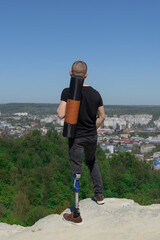 a man on a prosthetic leg travels the mountains. Dressed in black jeans and a T-shirt, he carrying...
