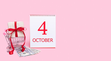 A gift box in a shopping trolley, dollars and a calendar with the date of 4 october on a pink background.