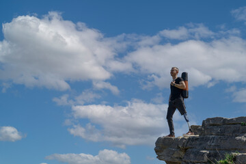 a man on a prosthetic leg travels the mountains. Dressed in black jeans and a T-shirt, he carrying mat