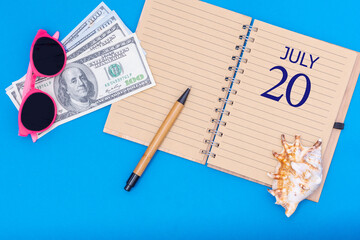 Travel concept flat lay - notepad with the date of 20 july pen, glasses, dollars and seashell on blue background.