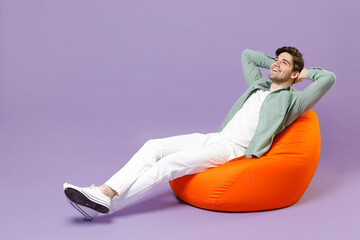 Full length fun man 20s in casual mint shirt white t-shirt sitting in orange bean bag chair hold...