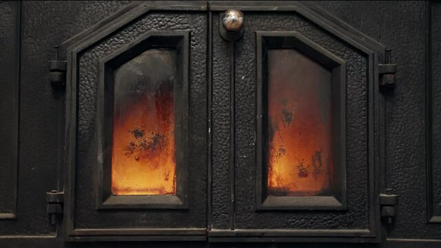 Close up on iron fireplace with metal doors. Wood slowly burning inside. Fire going in stove. Hot temperature warming up cabin or house. Romantic and intimate cozy feeling in winter or cold weather