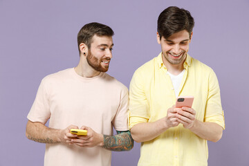 Young smiling curious happy men friends together wear casual t-shirt tattoo translate fun hold mobile cell phone chat online peeps isolated on purple background People lifestyle friendship concept