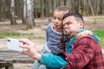 Dad and his little daughter take funny selfies in nature.