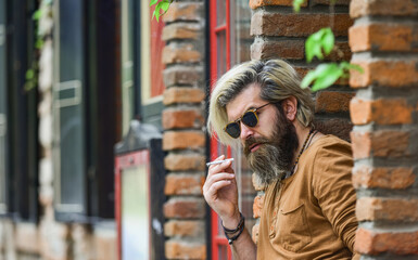 brutal mature hipster smoking cigarette. bad habits concept. harmful for your health. smoke nicotine addicted. he is heavy smoker. bearded man in glasses relax with cigarette