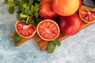 Sliced and whole ripe juicy Sicilian blood oranges on wooden cutting board with mint, blue concrete...