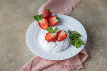 Mini Pavlova meringue cakes with strawberries and mint on a plate, concrete background.