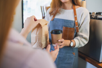 A waitress holding and serving coffee and a takeaway food in paper bag to customer in a shop