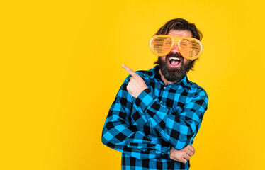 happy bearded man wearing funny party glasses and pointing finger on yellow background, copy space, best offer