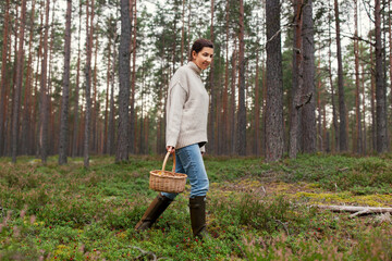 picking season and leisure people concept - young woman with mushrooms in wicker basket walking in forest
