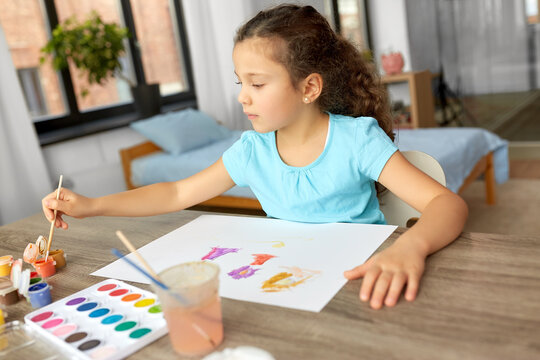 childhood, hobby and leisure concept - little girl drawing picture with colors and brush at home