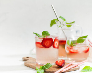 Homemade refreshing strawberry lemonade in glasses and jug with fresh strawberries and mint leaves. Summer drink 