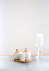 Bright containers of salt, pepper and sugar made from ceramics. White candle on a candle stick. Objects on a table. Selective focus on the small container in front, blurred background.