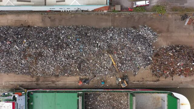 Birdseye drop down over a large pile of scrap metal being loaded onto a ship