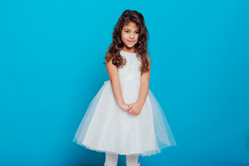 Obraz na płótnie Canvas Beautiful little curly girl 5 years old in a white dress on a blue background