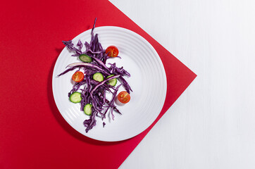Fresh summer vegetable salad with red cabbage, cherry tomato, cucumber with shadow in sunny day on red color, white wood table, top view.
