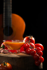 típico tazón de gazpacho con pimientos y tomates frente a una guitarra española - 434065640