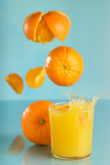 Naranjas y trozos cayendo en un vaso de zumo de naranja - 434065698