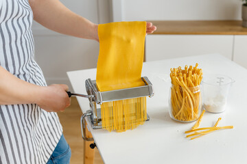 Man in apron making spaghetti with noodle cutter. Close-up pasta cooking at home. Preparing food from bright yellow dough
