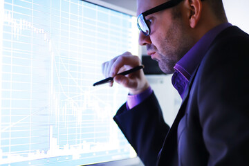 A businessman is looking at a graph on a monitor. An exchange broker evaluates stock market trends. A man with glasses in front of a curve of the dynamics of the economy.