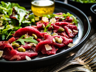 Beef carpaccio  with parmesan, capers, and arugula on wooden table
