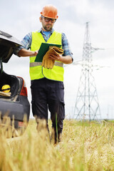 A man in a helmet and uniform, an electrician in the field. Professional electrician engineer inspects power lines during work.