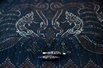Spool of thread with traditional Thai silk fabric pattern as background. 