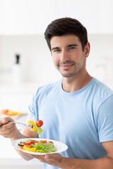 Handsome young man eating healthy food during lunch break with plate enjoying vegetables.