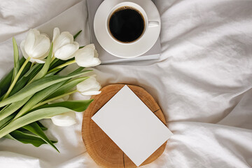 Coffee, white tulips and empty paper card on the bed