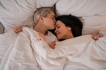 top view of lesbian couple lying in bed under blanket